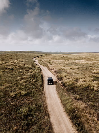 A vehicle travels on a winding dirt road through rural Caboledo, Angola. HD phone wallpaper
