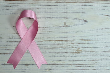 A pink ribbon symbolizing cancer awareness placed on a light wooden background. HD wallpaper
