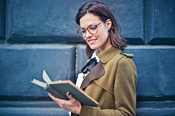 Smiling woman enjoying a book while standing against a textured blue wall. HD wallpaper