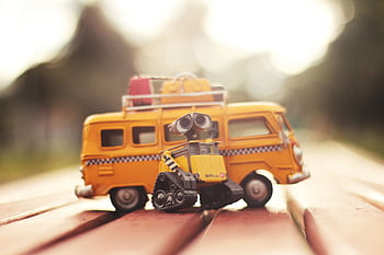 Charming miniature robot with yellow van toy in blurred outdoor daylight, capturing playful leisure theme. HD wallpaper