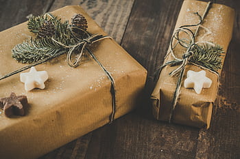 Two eco-friendly Christmas presents wrapped in brown kraft paper with pine decorations on a wooden table. HD wallpaper