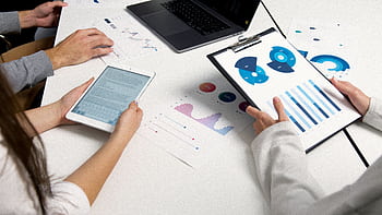 Team analyzing financial charts and digital reports during a business meeting. HD wallpaper