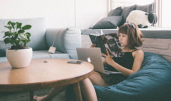 Woman reading while using a laptop in a cozy living space with modern decor. HD wallpaper