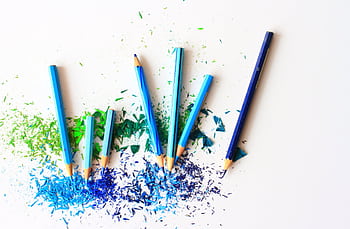 Creative display of colored pencils and vibrant shavings on a white background. HD wallpaper