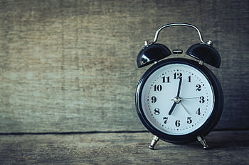 Classic black analog alarm clock on rustic wooden background, perfect for time and nostalgia themes. HD wallpaper