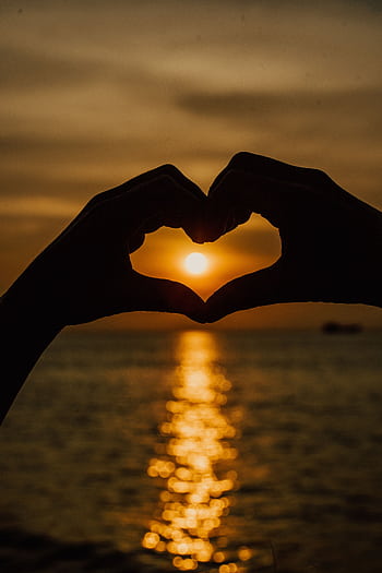 Silhouetted hands form a heart shape against a stunning ocean sunset backdrop. HD phone wallpaper