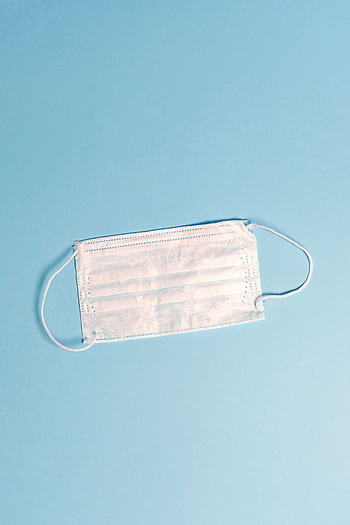 A disposable face mask on a light blue surface, symbolizing health and safety. HD phone wallpaper