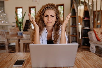 A woman frustrated with her laptop while working remotely indoors, expressing stress. HD wallpaper