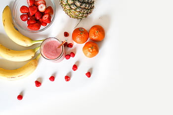A vibrant flat lay of tropical fruits including bananas, strawberries, and a smoothie on a white background. HD wallpaper