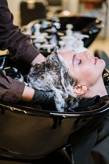 Professional hair stylist washing woman's hair in a modern salon setting. HD phone wallpaper