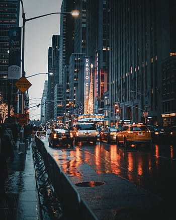 Dramatic city street view of New York's Radio City at night with reflections and taxis. HD phone wallpaper