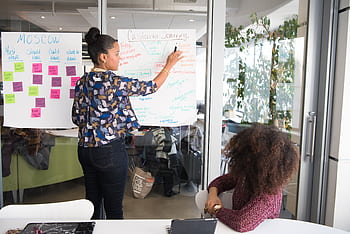 Two women collaborating on project strategy using notes in modern office. HD wallpaper