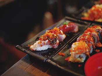 Appetizing sushi rolls with toppings served on a black plate, showcasing vibrant colors. HD wallpaper