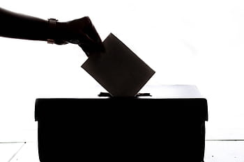 Silhouette of a hand placing a vote into a ballot box, symbolizing democracy. HD wallpaper