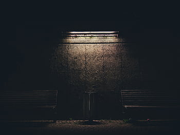Dark urban night scene with benches and a fluorescent lamp casting soft light on the wall. HD wallpaper