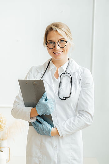 Portrait of a smiling female doctor in a lab coat with stethoscope and clipboard indoors. HD phone wallpaper
