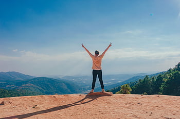 A woman stands victoriously on a mountain top with arms raised, embracing nature and dom. HD wallpaper