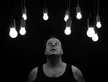 A man looks up thoughtfully at multiple illuminated light bulbs on a dark background. HD wallpaper