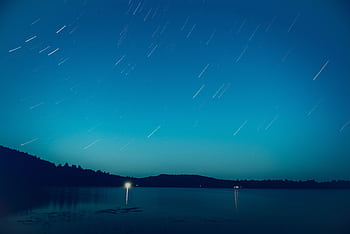 Long exposure of star trails over a lake in Barry's Bay, Canada, creating a serene night scene. HD wallpaper