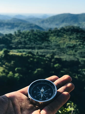 A handheld compass over majestic green mountains under blue skies, ideal for travel themes. HD phone wallpaper