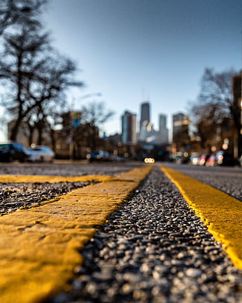 Dramatic low-angle shot of an urban street with blurred city skyline under clear blue sky. HD phone wallpaper