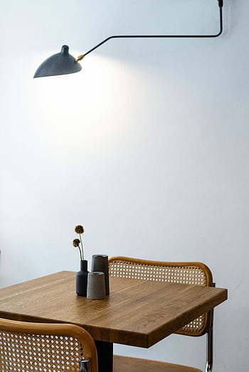 A minimalist interior showcasing a wooden table, two chairs, and a modern wall lamp, perfect for contemporary home decor. HD phone wallpaper