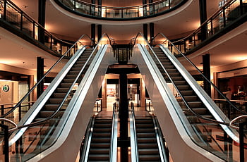 Symmetrical view of escalators in a modern shopping mall interior, showcasing architecture and design. HD wallpaper