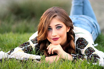 Fashionable young woman with braided hair lying on grass, showcasing a vibrant look. HD wallpaper