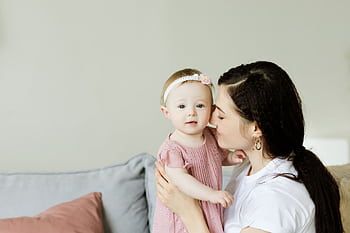 Tender moment of a mother kissing her baby daughter. Warm and loving family scene indoors. HD wallpaper