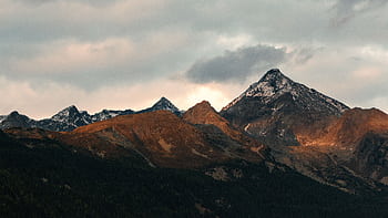 Breathtaking view of mountain peaks adorned with snow under a cloudy sky at dusk. HD wallpaper