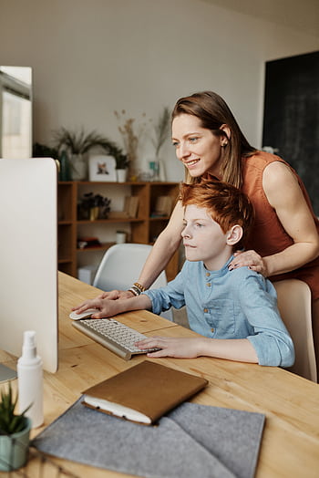 A mother helps her son with online learning on a home computer. HD phone wallpaper