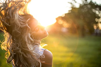 A young woman tosses her long, wavy blond hair in the sunlight during golden hour outdoors. HD wallpaper