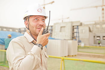 Male construction worker using radio on a building site, wearing a safety helmet, communicating effectively. HD wallpaper