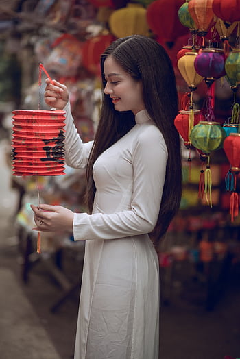 Woman in traditional dress holding lantern in vibrant street market. Captivating cultural scene. HD phone wallpaper