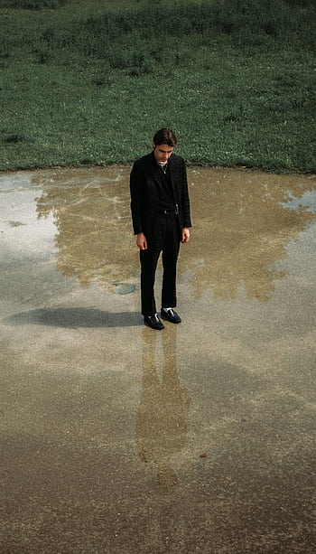 A man in a suit stands contemplatively by a puddle, reflecting on his thoughts. HD phone wallpaper