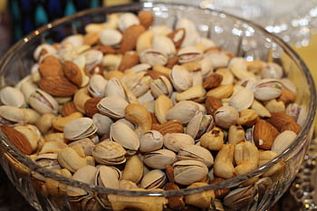 A close-up view of a glass bowl filled with various mixed nuts, including almonds, cashews, and pistachios. HD wallpaper
