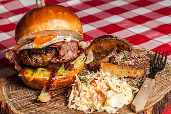 Delicious gourmet burger with bacon, cheese, coleslaw, and potato wedges on a rustic board. HD wallpaper