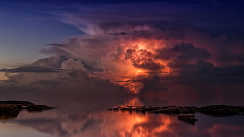 A stunning sunset scene depicting a dramatic stormy seascape with vivid lightning reflecting over calm waters. HD wallpaper