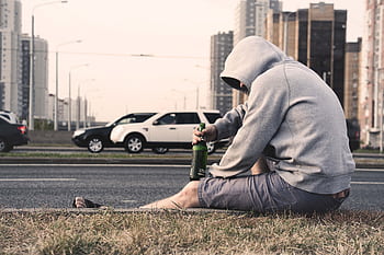 A man sits alone on the roadside in Moscow, holding a beer, reflecting urban loneliness. HD wallpaper