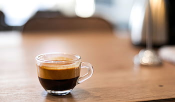 A close-up shot of freshly brewed espresso in a glass cup on a wooden table. HD wallpaper