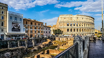 Daylight view of the historic Colosseum in Rome with vibrant city buildings. HD wallpaper