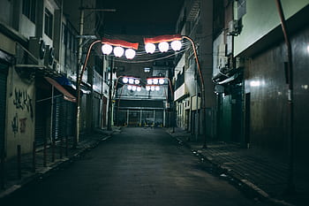 A deserted urban alley at night featuring unique red-lit hanging lights, creating a dramatic atmosphere. HD wallpaper