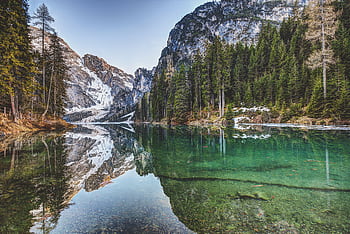 Tranquil lake reflecting snowy mountains and evergreen trees in a serene landscape. HD wallpaper