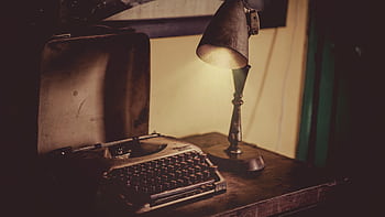 Cozy indoor setting with a vintage typewriter and antique lamp on a wooden desk, perfect for nostalgic themes. HD wallpaper