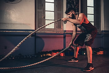 Man performing a challenging Crossfit rope exercise in an indoor gym setting. HD wallpaper