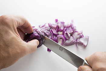 Close-up of hands slicing purple onions on a white cutting board with a sharp knife. HD wallpaper