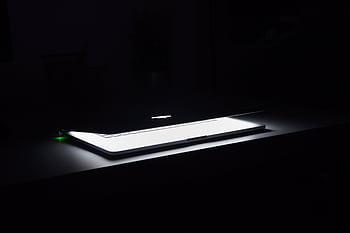 A dramatic, low-light of a slightly open laptop with glowing keys on a dark desk. HD wallpaper
