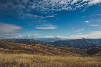Stunning view of rolling hills and mountains under a bright blue sky with clouds. HD wallpaper