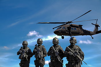 Special forces soldiers in tactical gear with helicopter overhead under a blue sky. HD wallpaper
