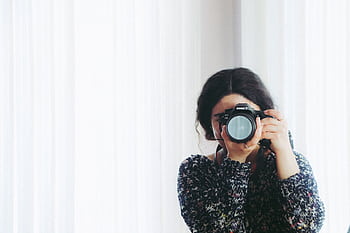 A young woman holding a camera indoors, capturing a in a modern setting. HD wallpaper